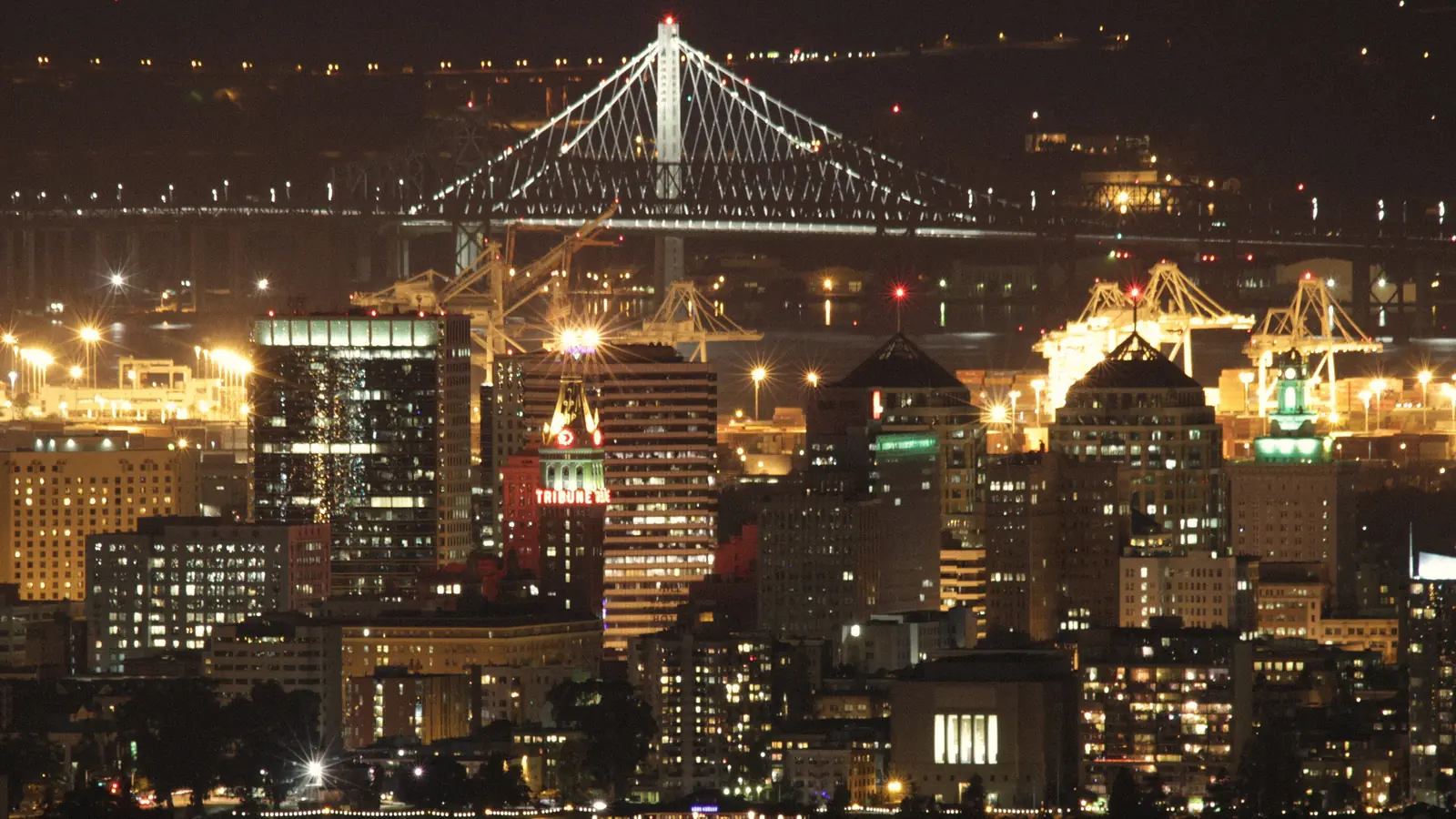 Photo of downtown Oakland towers and the Bay Bridge lit at night