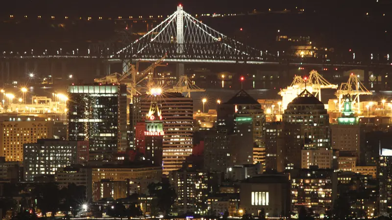 Photo of downtown Oakland towers and the Bay Bridge lit at night